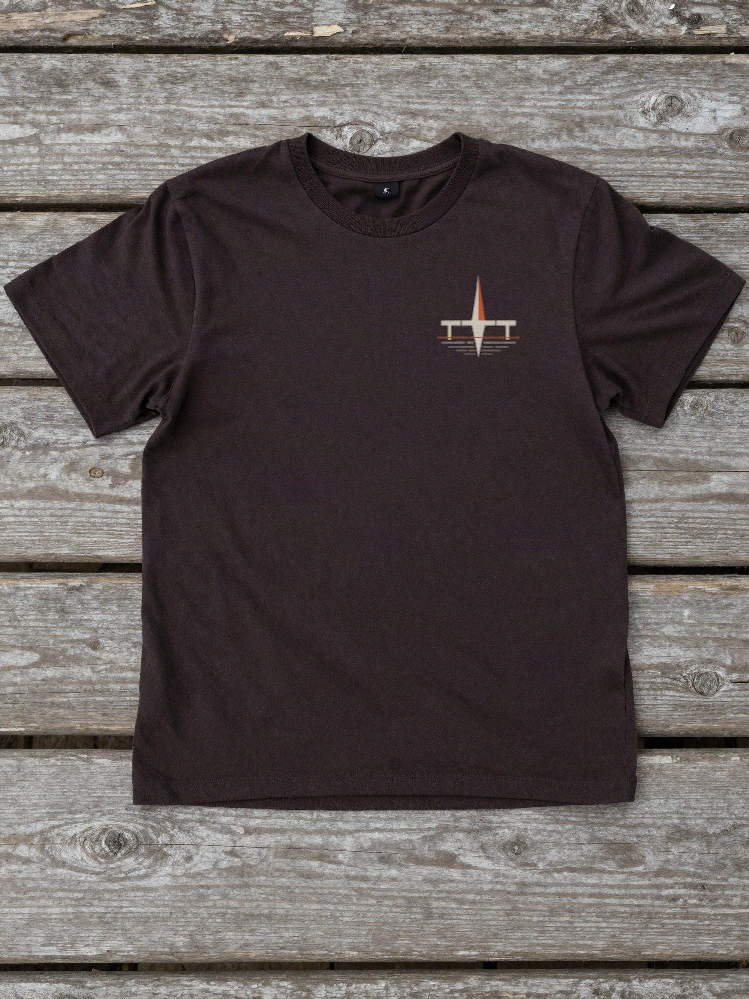 Camiseta escura estendida sobre tábuas com o símbolo 02 negativo pequeno no peito esquerdo