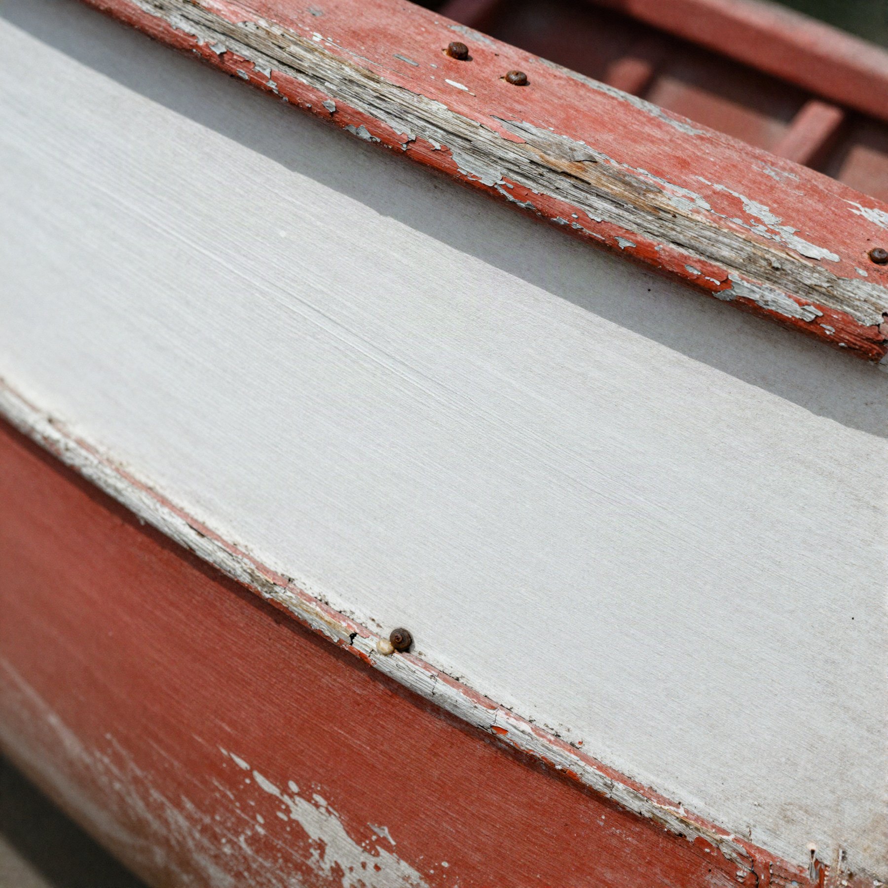 Detalhe de tábua de casco de barco caiada de branco, com o zarcão vermelho aparecendo sob a tinta descascada